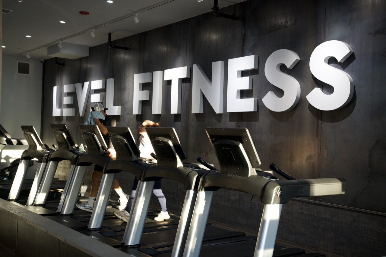 The illuminated LEVEL FITNESS wall above a row of treadmills at the Thornwood club